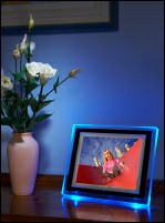 LCD photoframe on polished wood surface adjacent to vase of flowers.